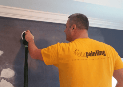 Painter sanding a patched wall below crown molding before painting in Des Plaines