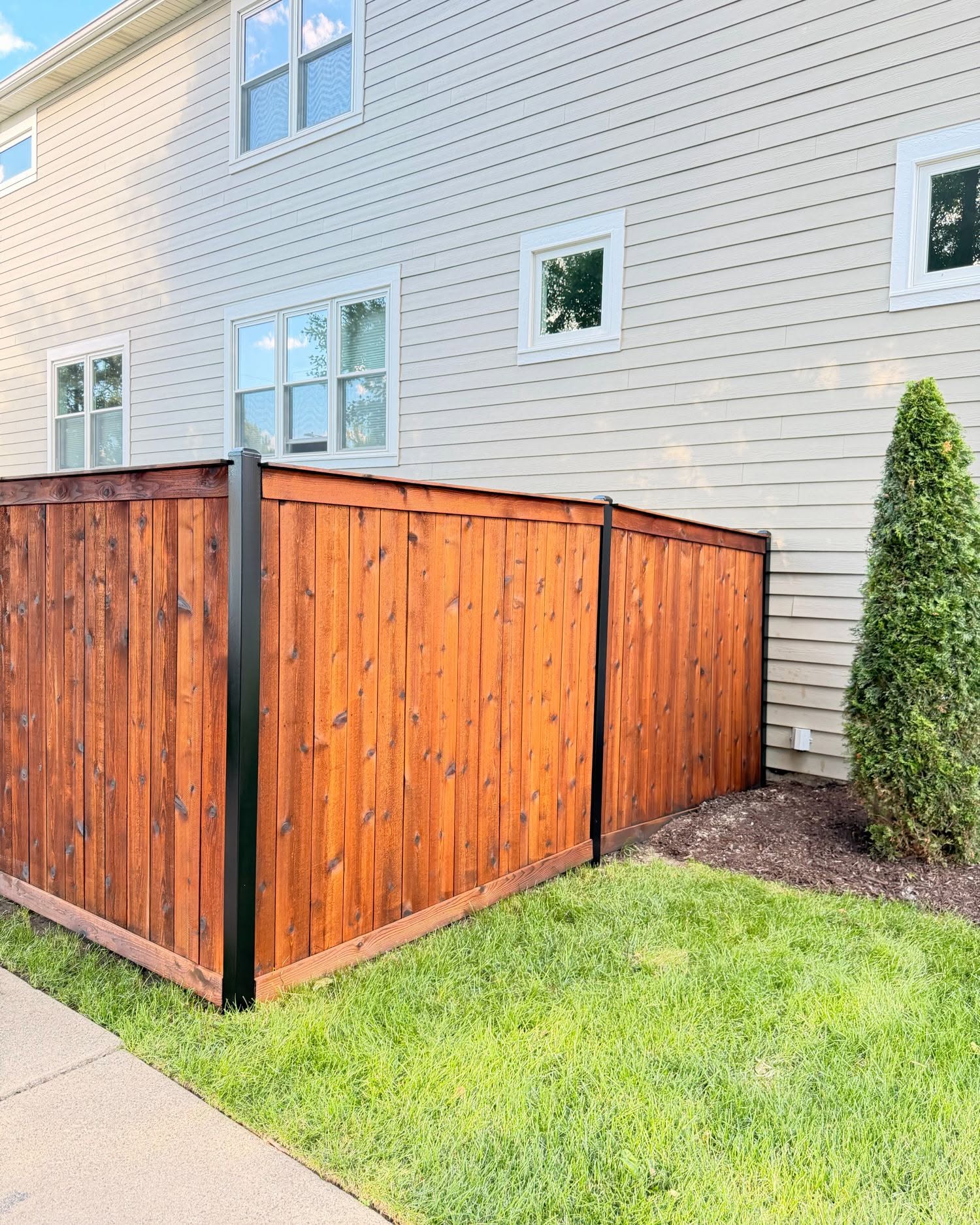 Completed cedar privacy fence staining in Chicago IL by Sunpainting, rich walnut finish with black metal posts and rails along side of home