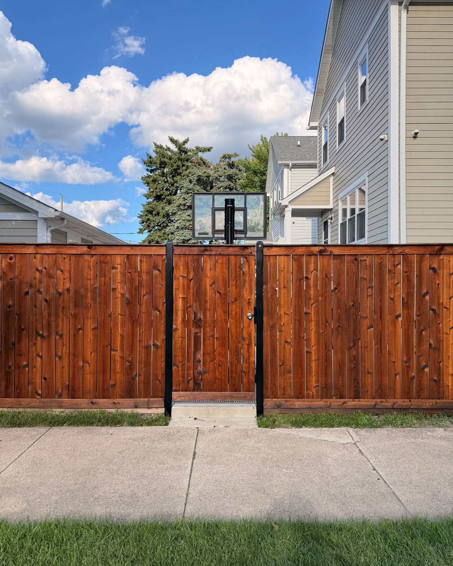 Stained cedar fence gate in Chicago IL, walnut semi-transparent stain with black metal post hardware after completion by Sunpainting