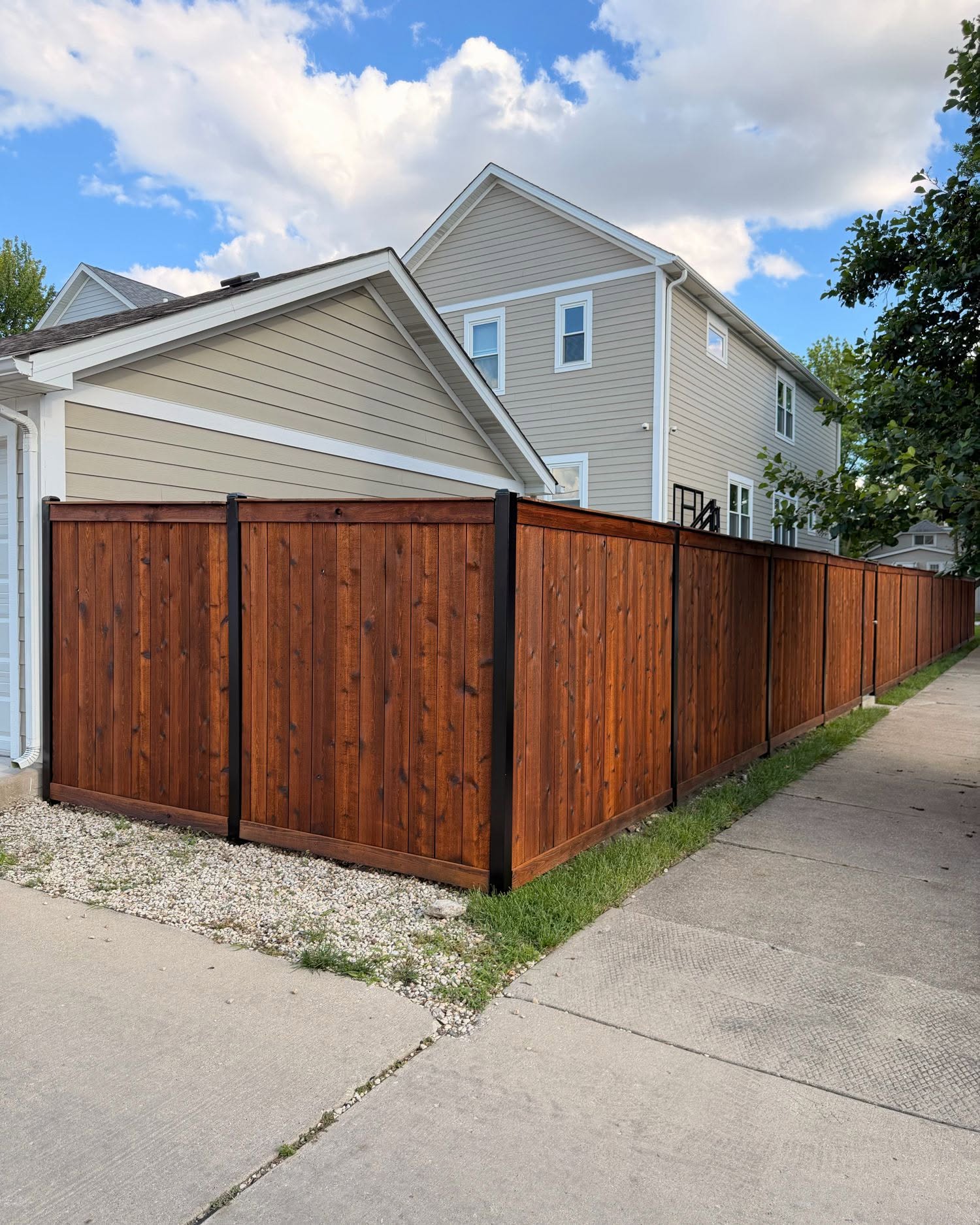 Full perimeter cedar fence staining completed in Chicago IL by Sunpainting, even walnut color across all panels and black metal posts