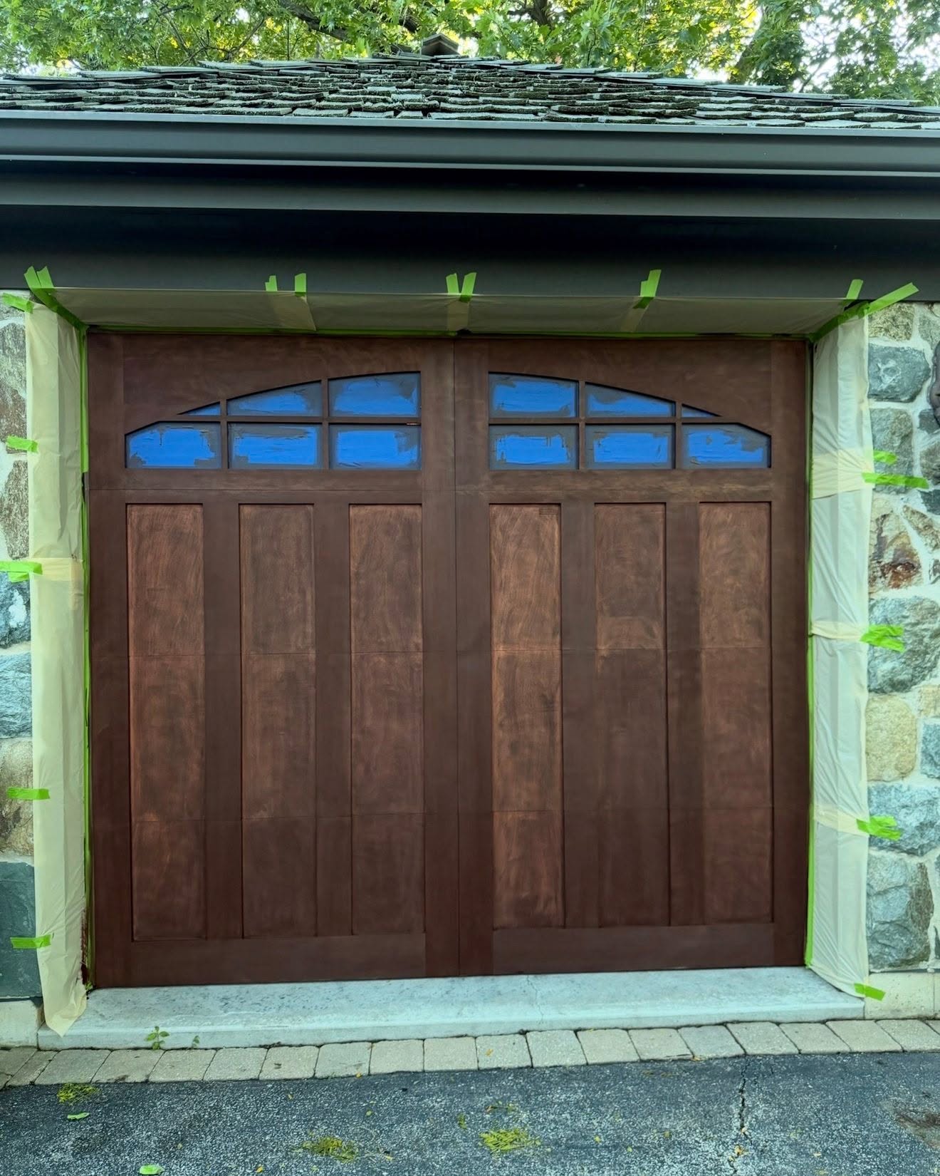 Mahogany stain being applied to wood garage door in Glenview IL, stone surround masked with green tape, Sunpainting exterior wood restoration