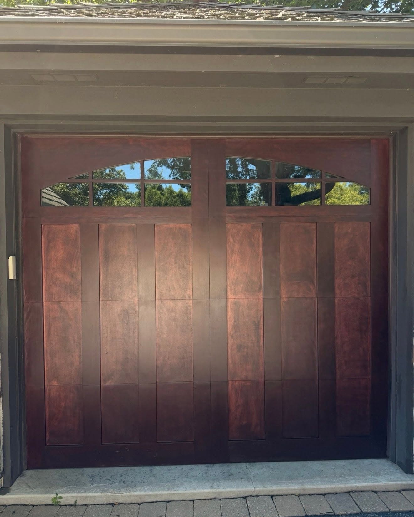 Completed wood garage door staining in Glenview IL by Sunpainting, deep mahogany finish with clear arched glass inserts and natural stone surround