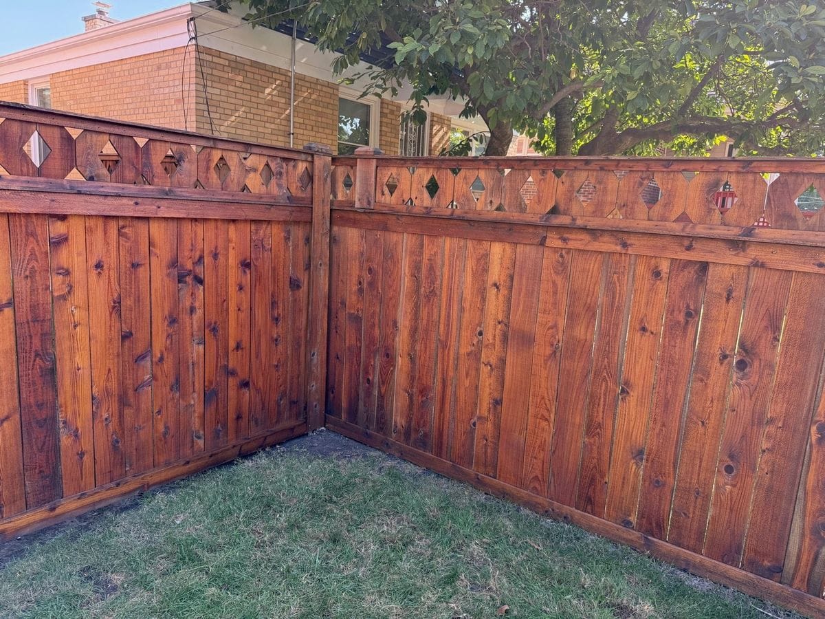 Stained wood fence corner with decorative diamond cutouts along the top, Sunpainting project