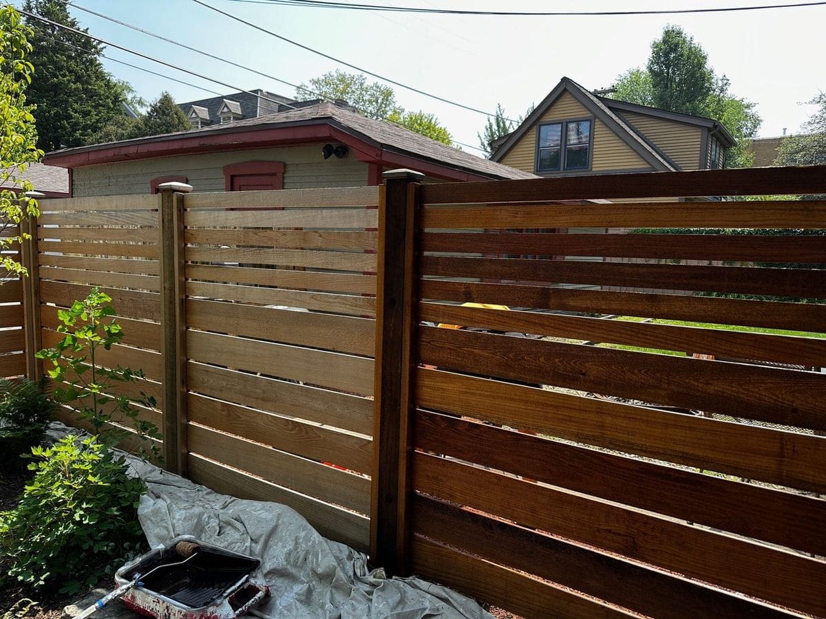 Stained horizontal-slat wood fence with a drop cloth protecting the ground beside it