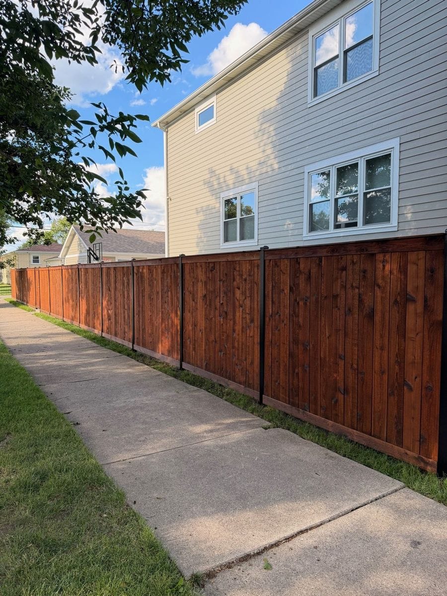 Long stained wood fence running along a backyard walkway next to a house