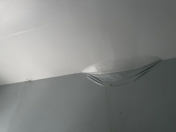 Water-damage bubble at the ceiling and wall corner of a bathroom before repair