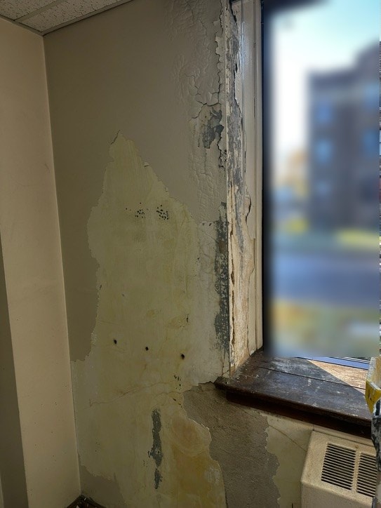 Peeling, cracked plaster on a wall beside a window before repair