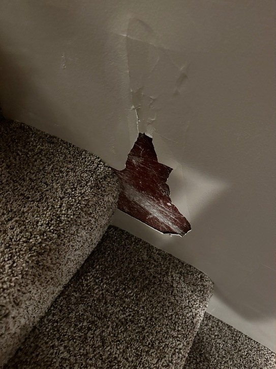 Torn hole in a drywall stairwell wall beside carpeted stairs before repair