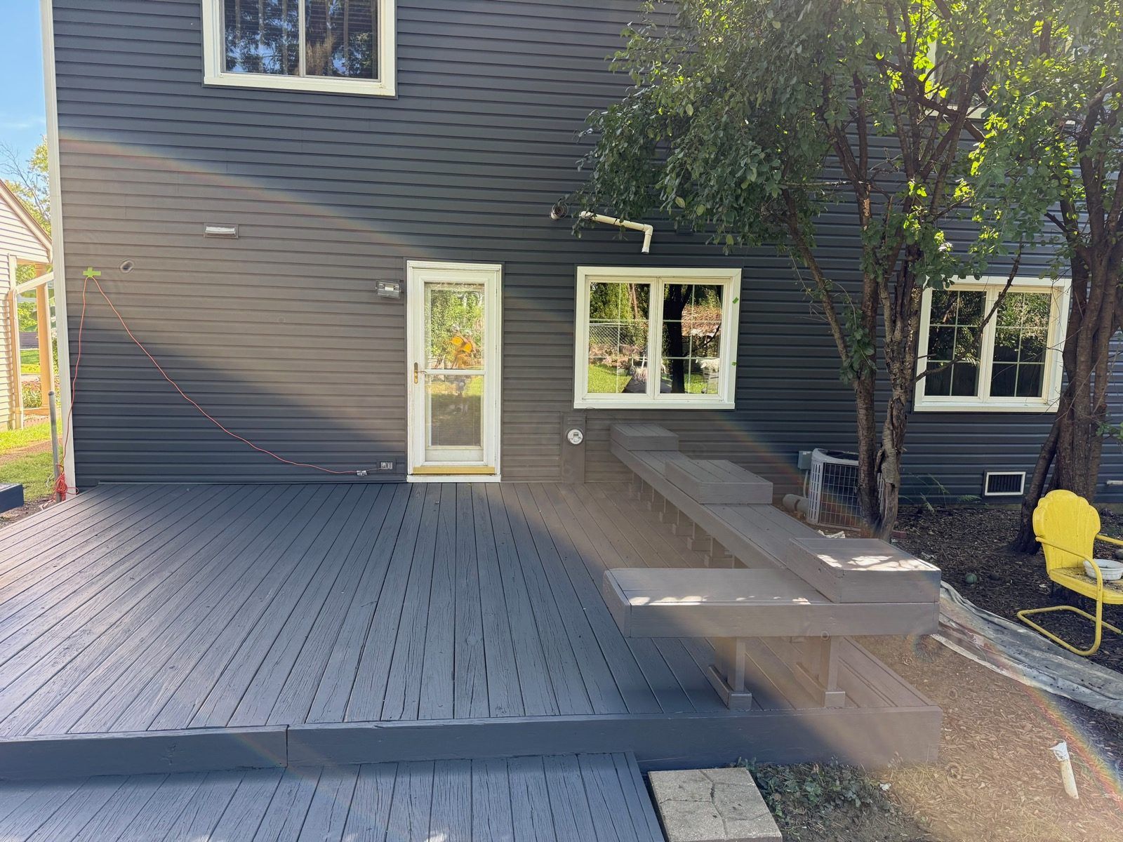 Refinished gray wood deck with a built-in bench behind a dark gray house Refinished gray wood deck with a built-in bench behind a dark gray house