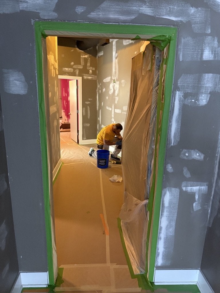 Sunpainting crew member patching a wall in a hallway protected with plastic sheeting and paper-covered floors