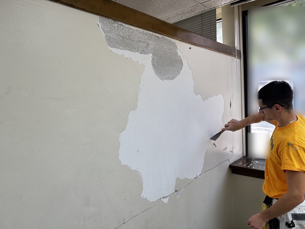 Sunpainting crew member scraping loose material off a wall with a putty knife